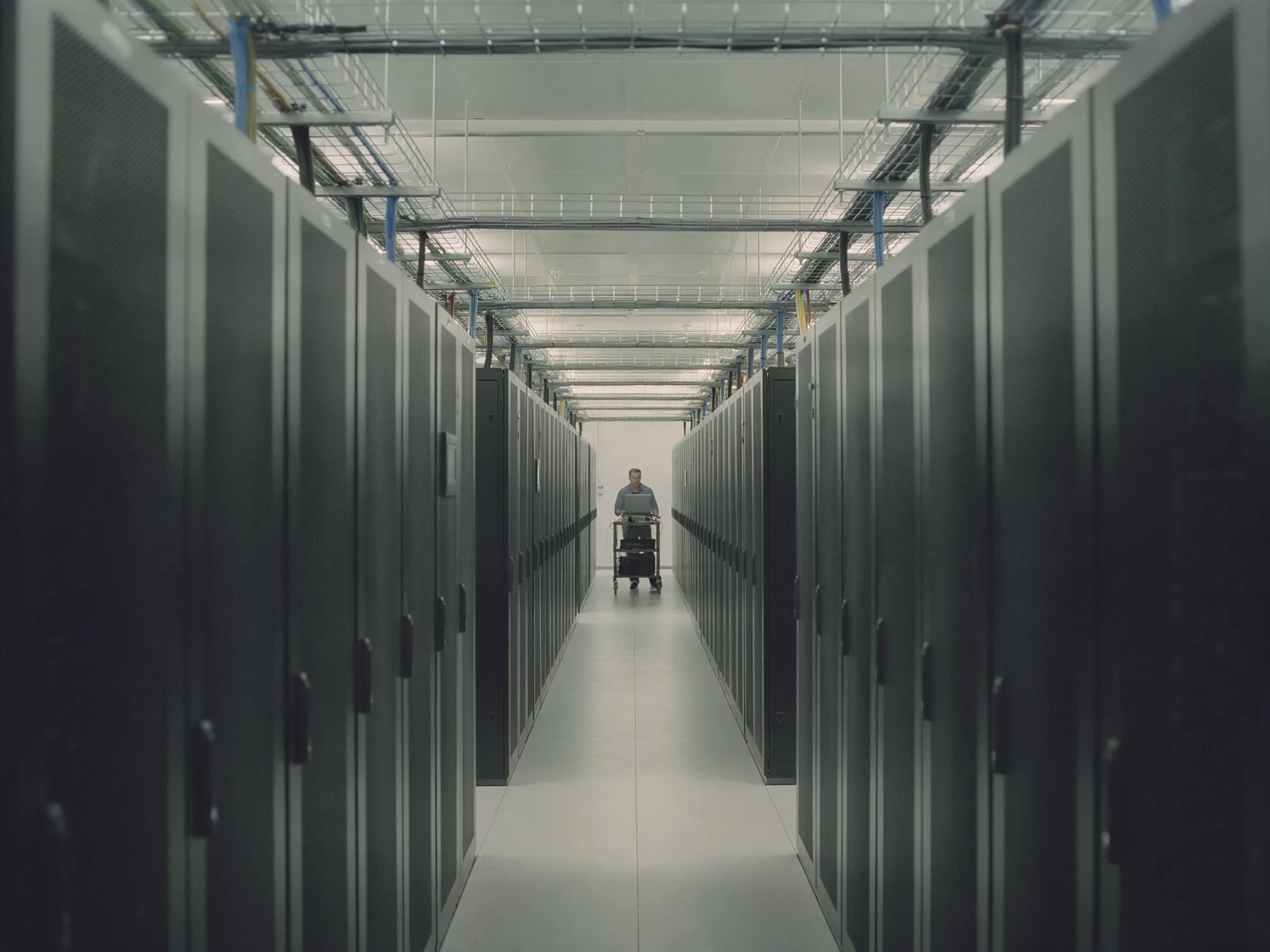 Ein Kaltgang zwischen Serverschränken in einem Rechenzentrum, ein Techniker weit hinten.